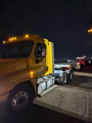 Yellow semi-truck with a flatbed trailer at night, headlights on.