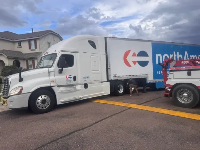White semi-truck with blue and red logo being towed. Dog near the trailer.