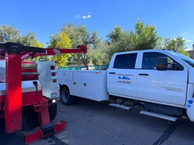 White work truck with red tow truck arm; blue sky, trees.