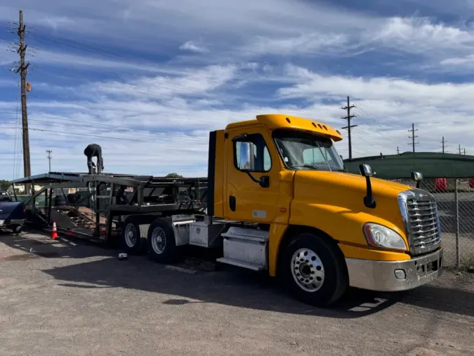 Yellow semi-truck with trailer; person on trailer. Outdoors, day, cloudy sky.