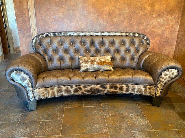 A brown leather couch with a pillow on it is sitting on a tiled floor.