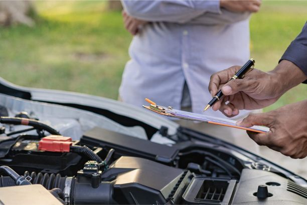 Mechanic inspecting car engine bay with a clipboard while another person stands nearby