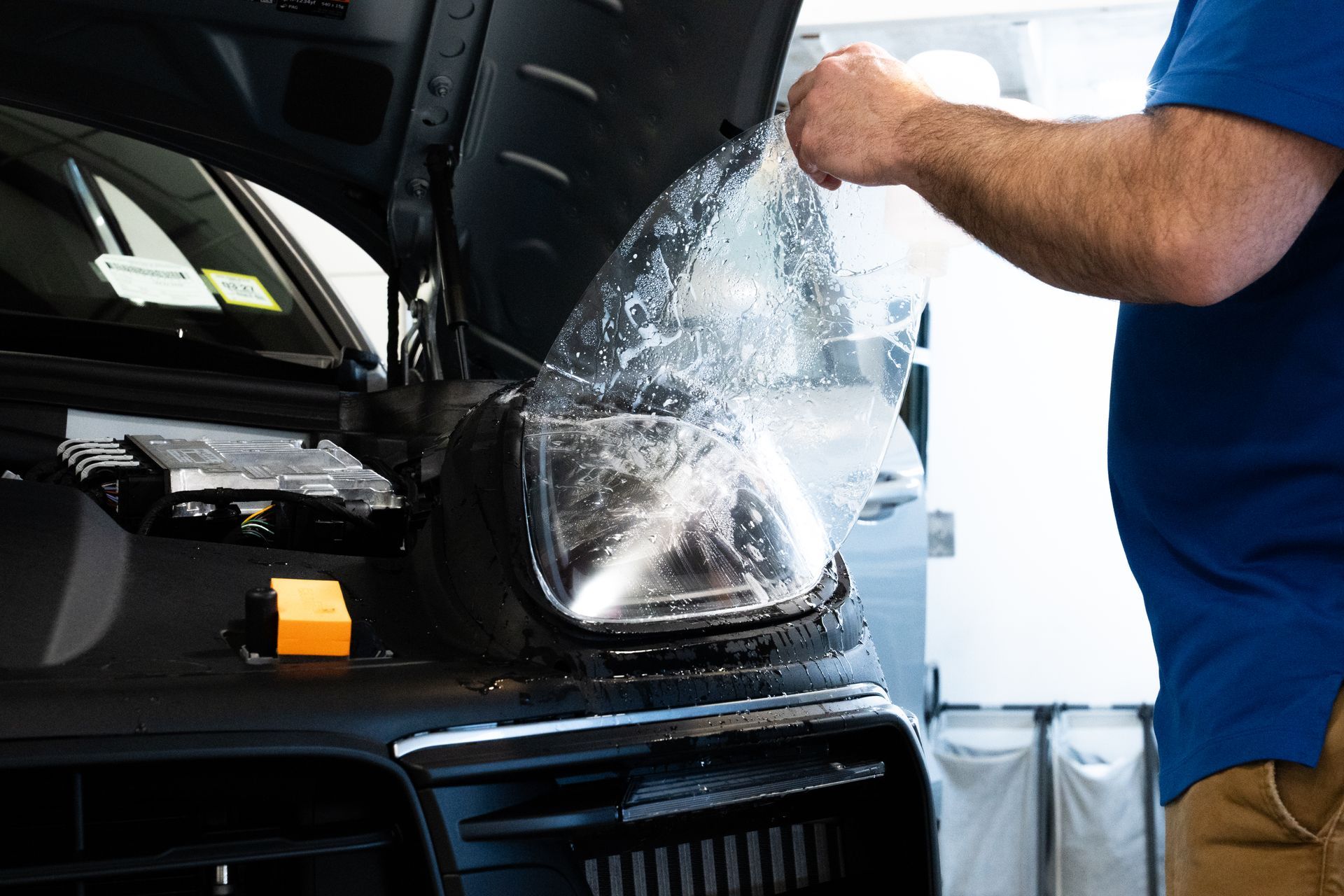 Car detailer spraying water on a black car’s headlight in a garage