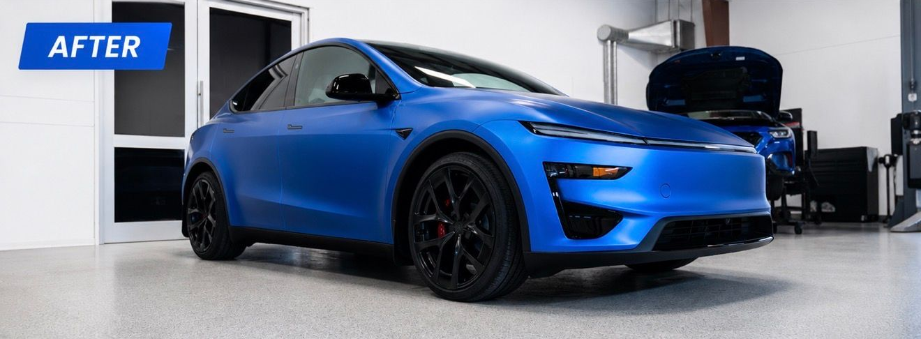 Blue sports car in a garage, shown after detailing, with glossy black wheels and an open hood.