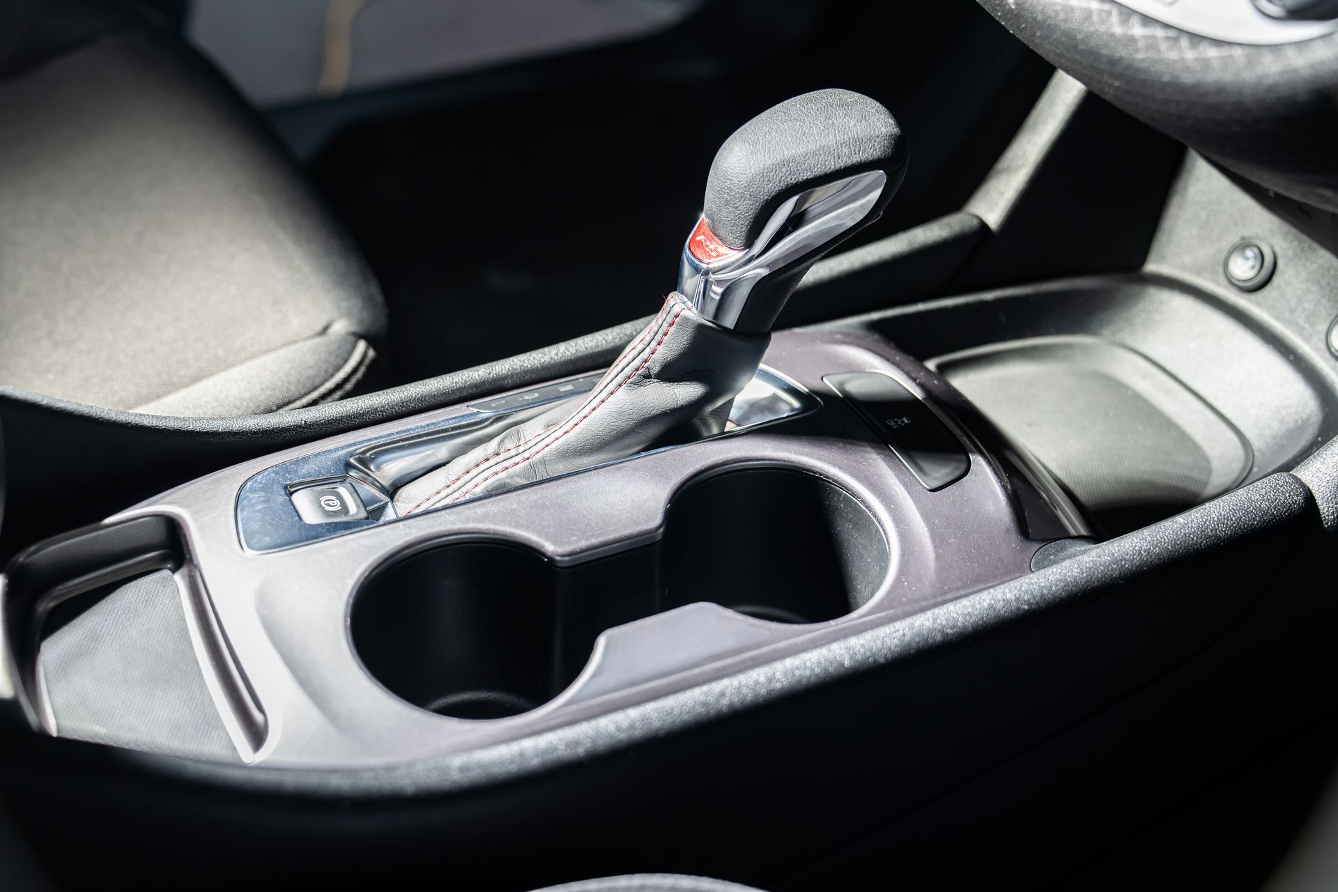 Car cup holder and gear shifter in a car interior, with black trim and silver accents