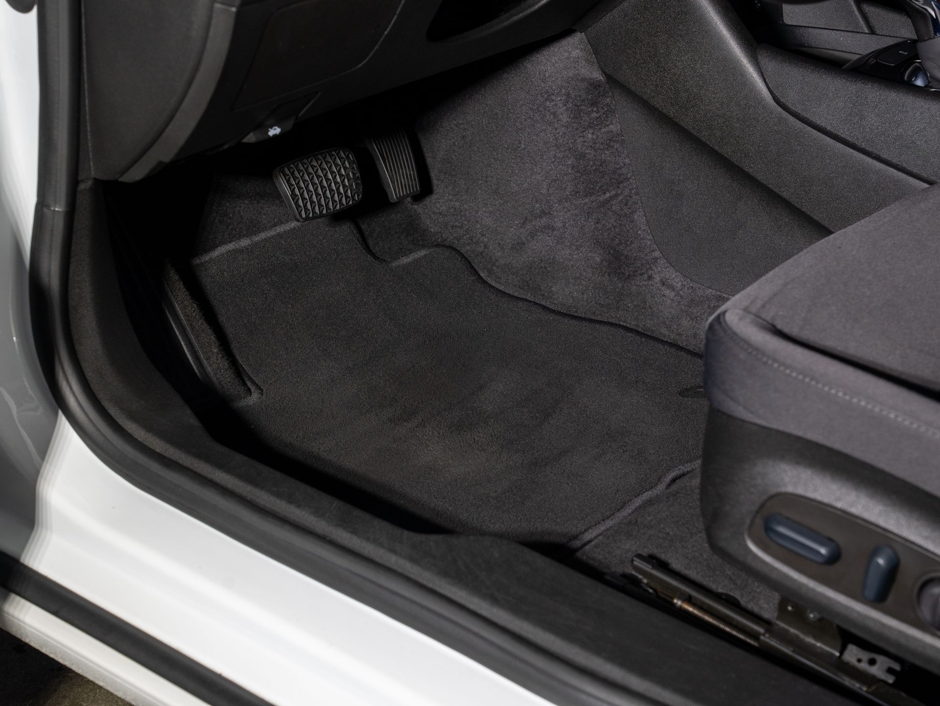 Car interior footwell with black floor mat and side seat controls visible on the right