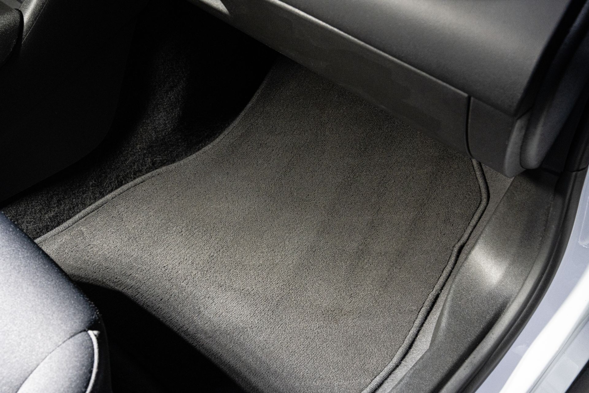 Car floor mat on the passenger side, dark gray carpet in a car interior