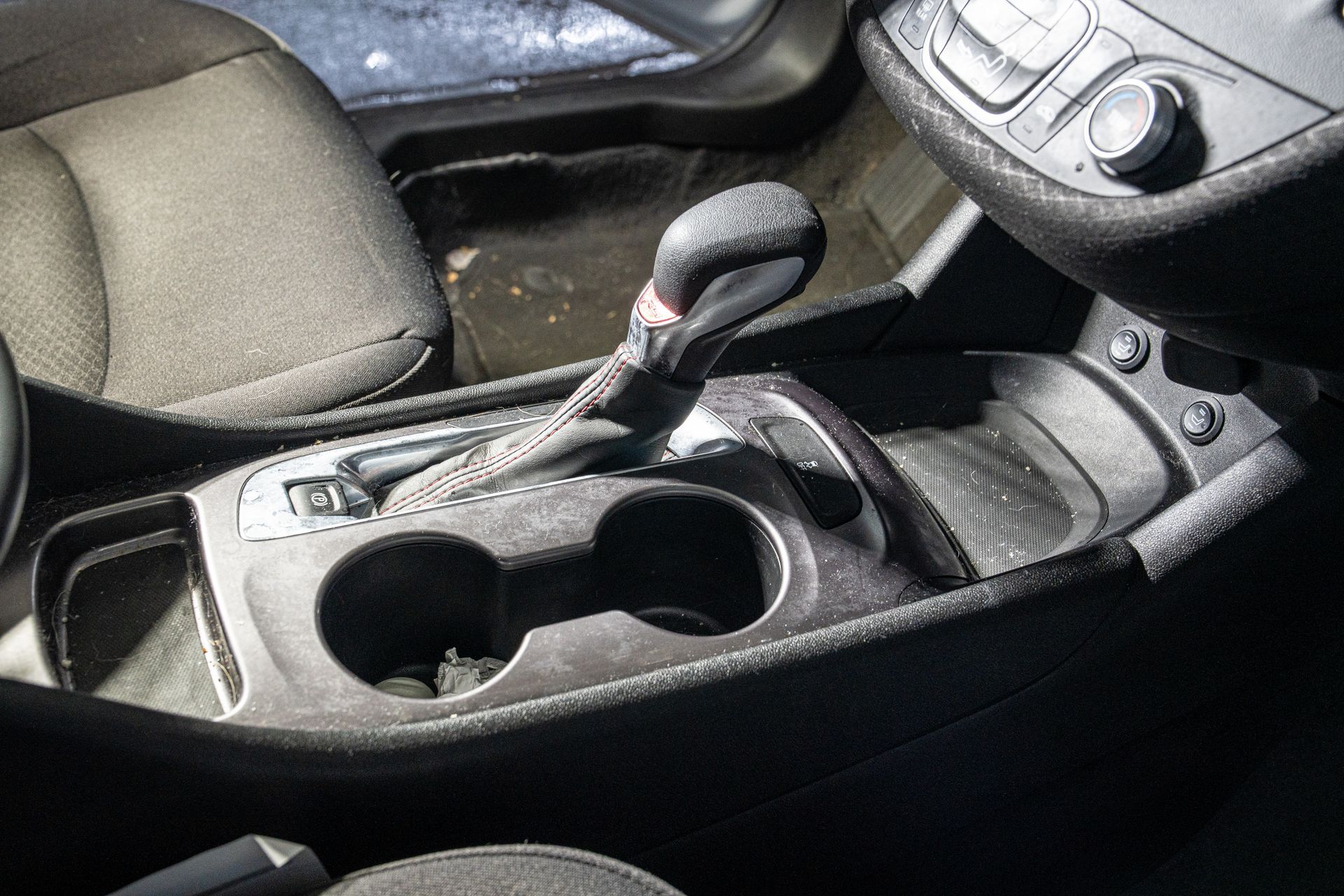 Car’s center console with gear shifter, cup holders, and control buttons in a dark interior