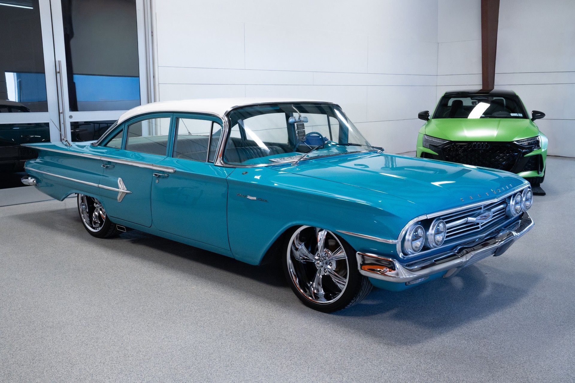 Turquoise classic car in a showroom, with a green sports car in the background