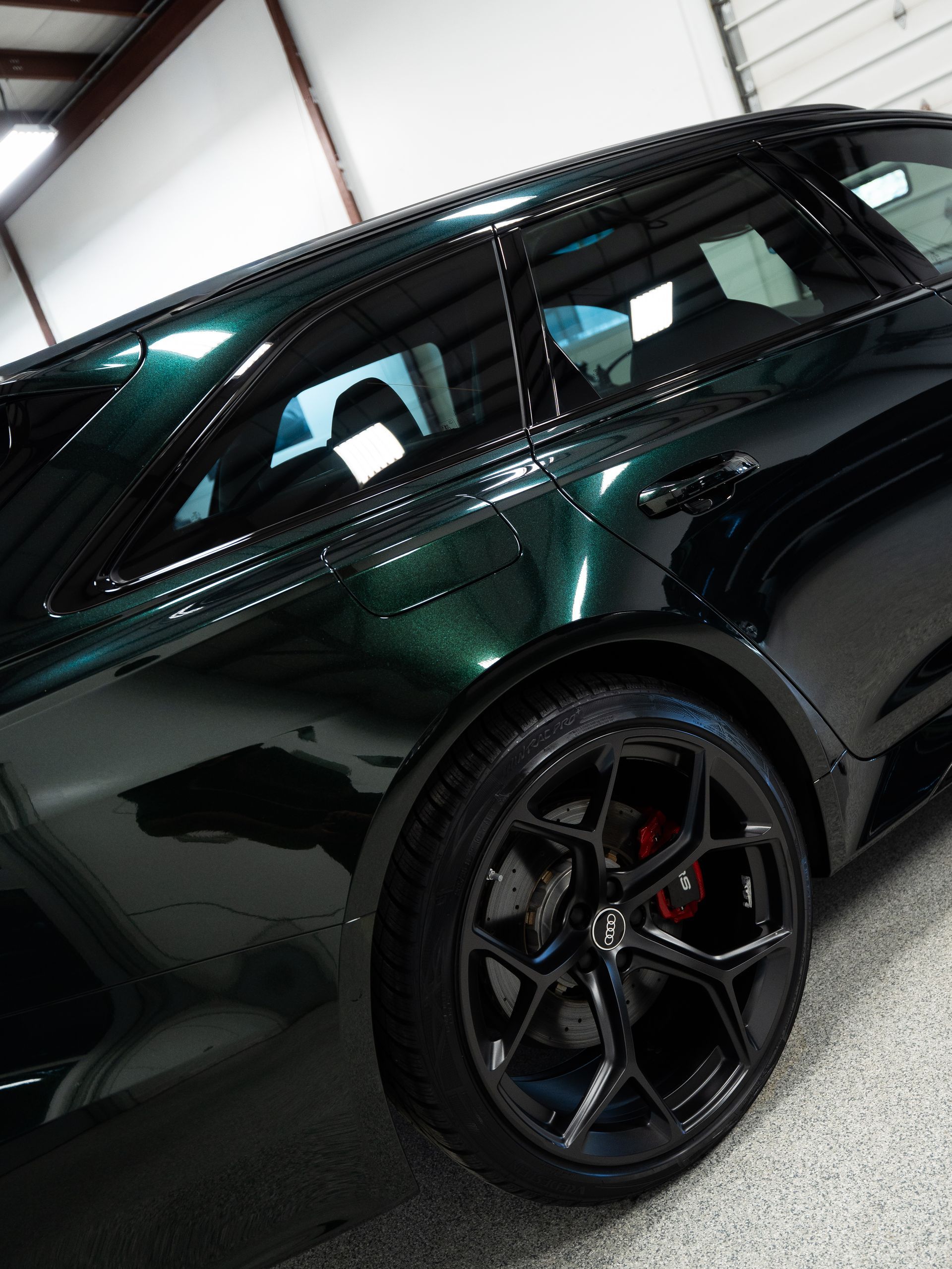 Black sports car in a garage, shown from the rear side with glossy paint and black wheels.