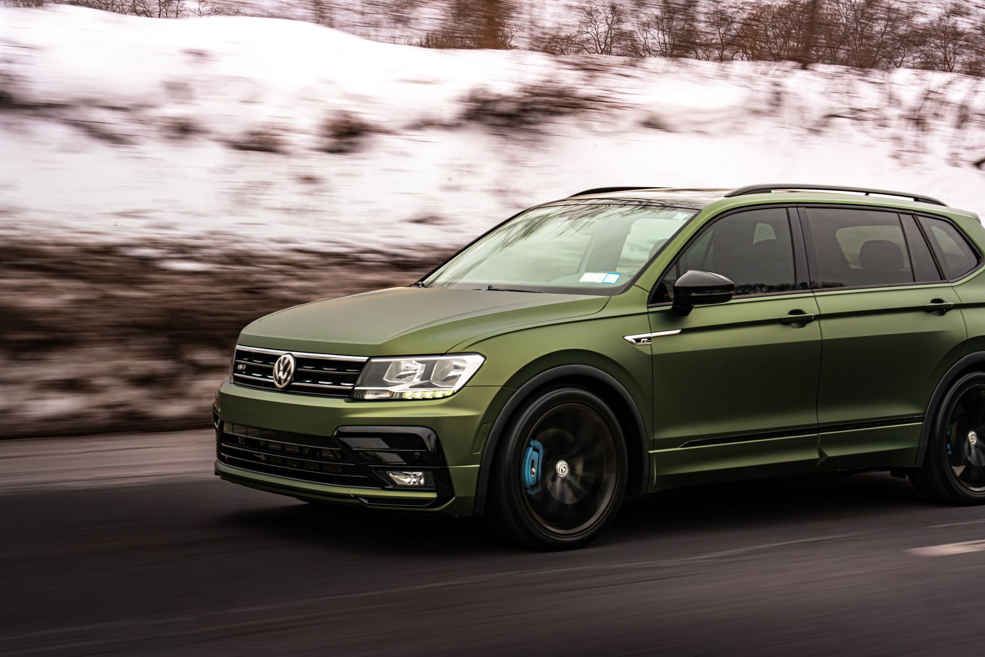 Olive green SUV driving on a snowy road with motion blur in the background