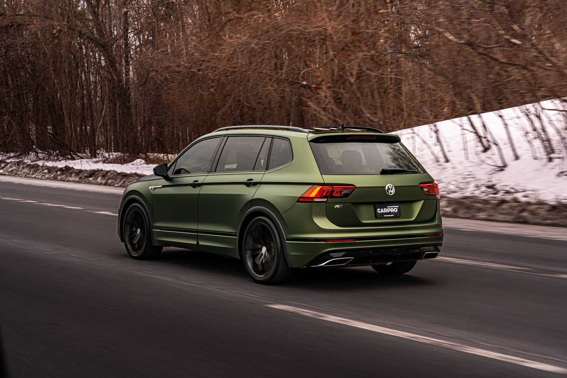 Green SUV driving on a wet road beside a snowy forest hillside