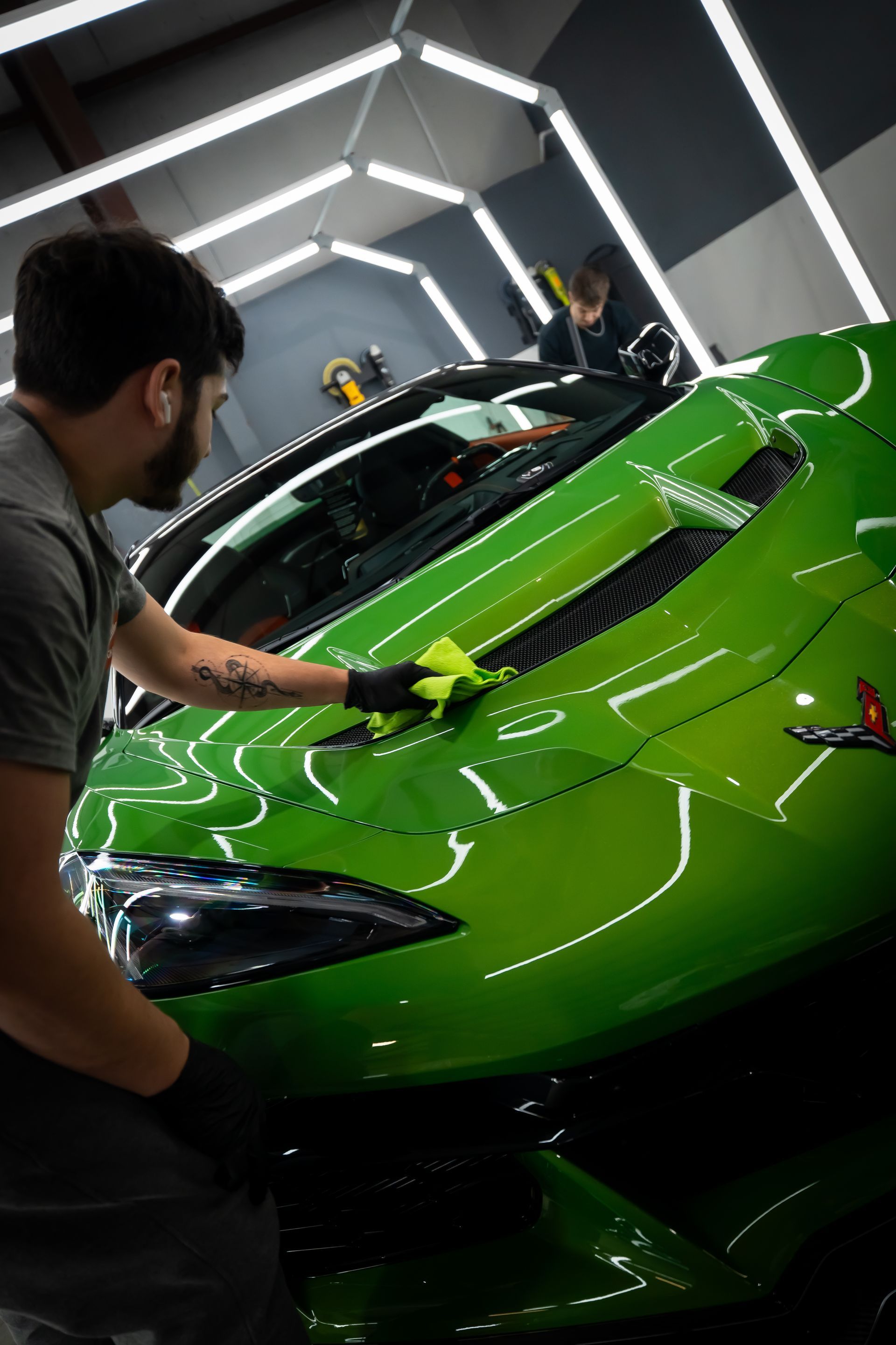 Worker polishing a bright green sports car in a showroom-like garage.