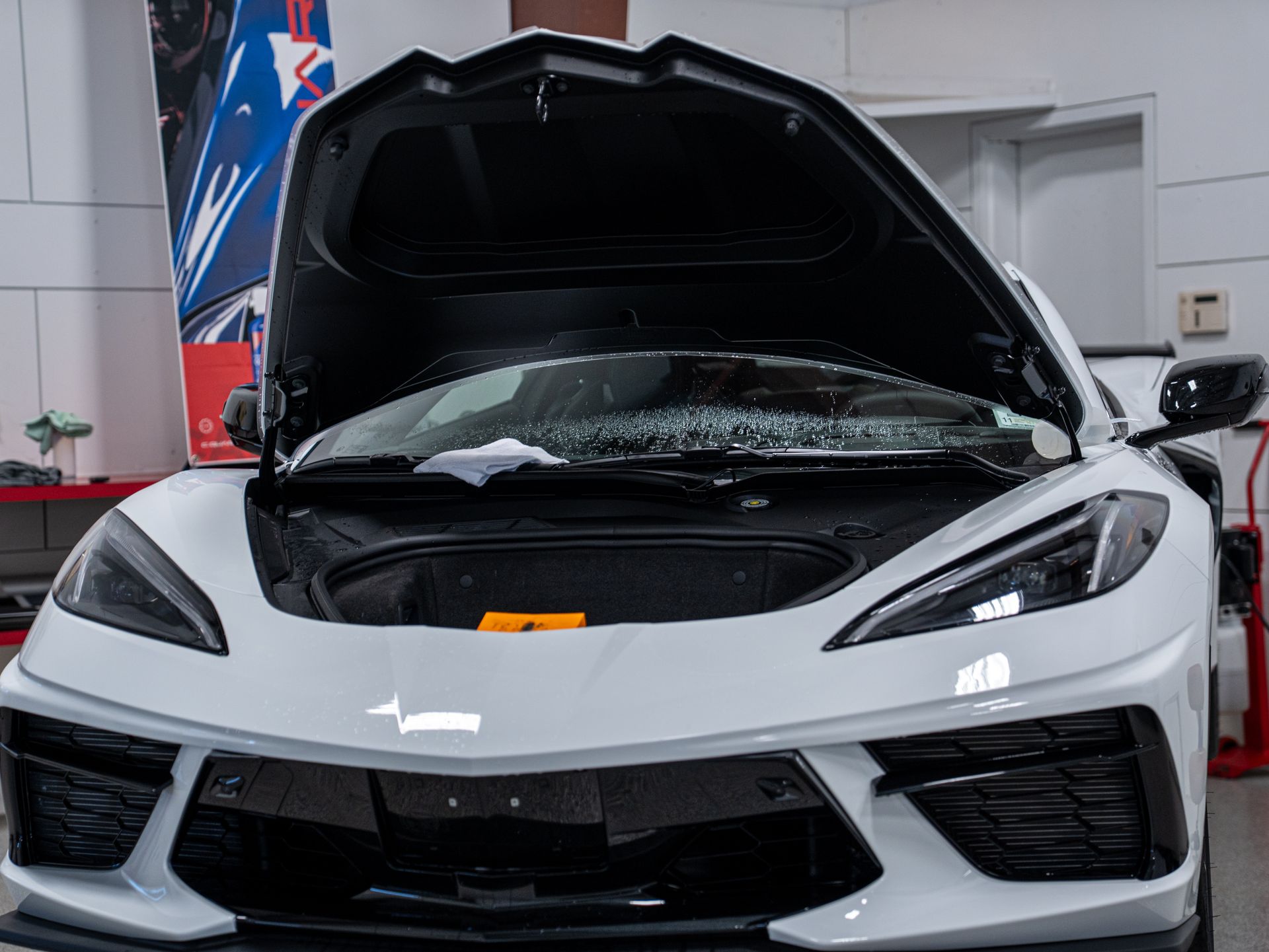 White sports car with hood open in a garage, showing the front end and engine bay