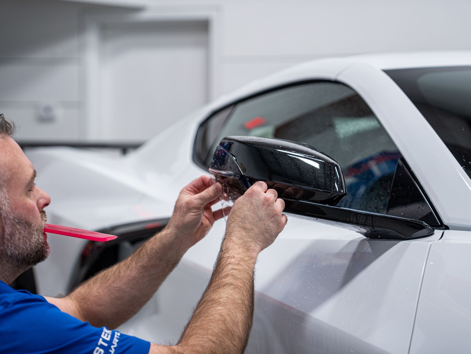 Technician installing a black side mirror on a white car in a workshop