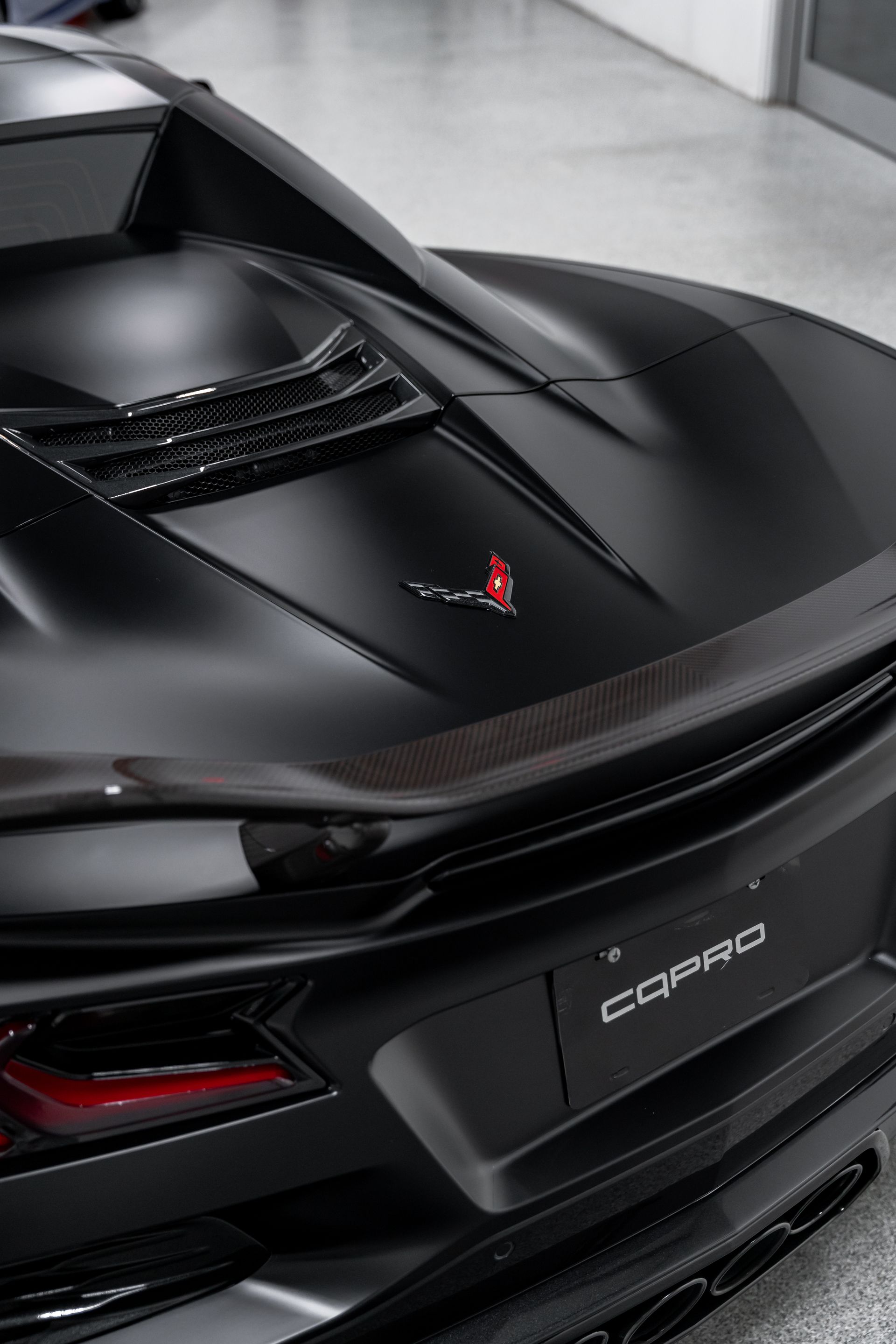 Black Chevrolet Corvette sports car rear in a showroom, with carbon-fiber details and C8 badge