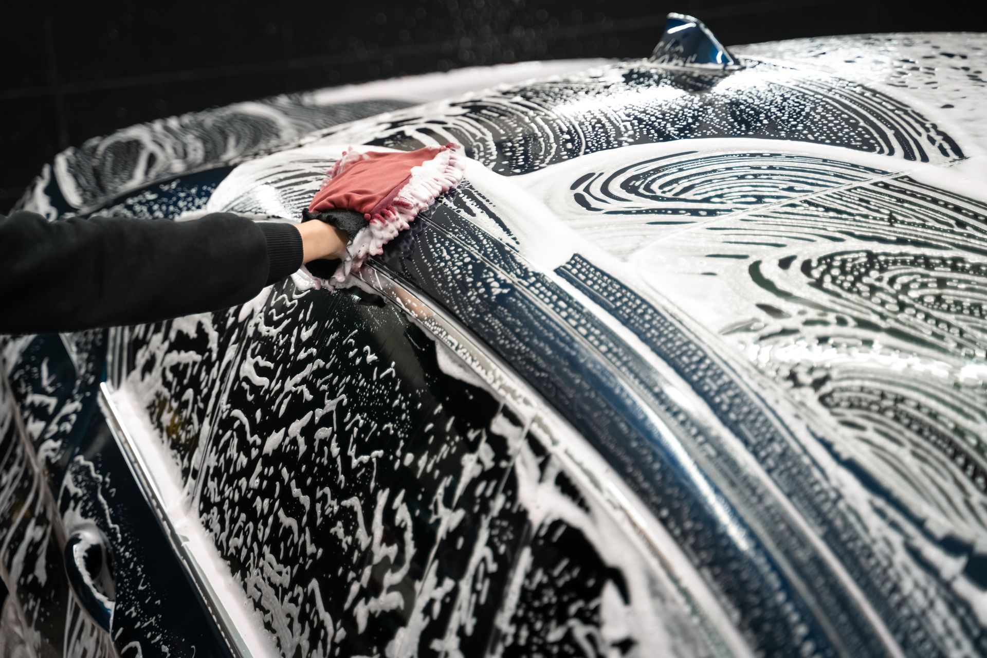 Person washing a car roof with soap suds and a red sponge