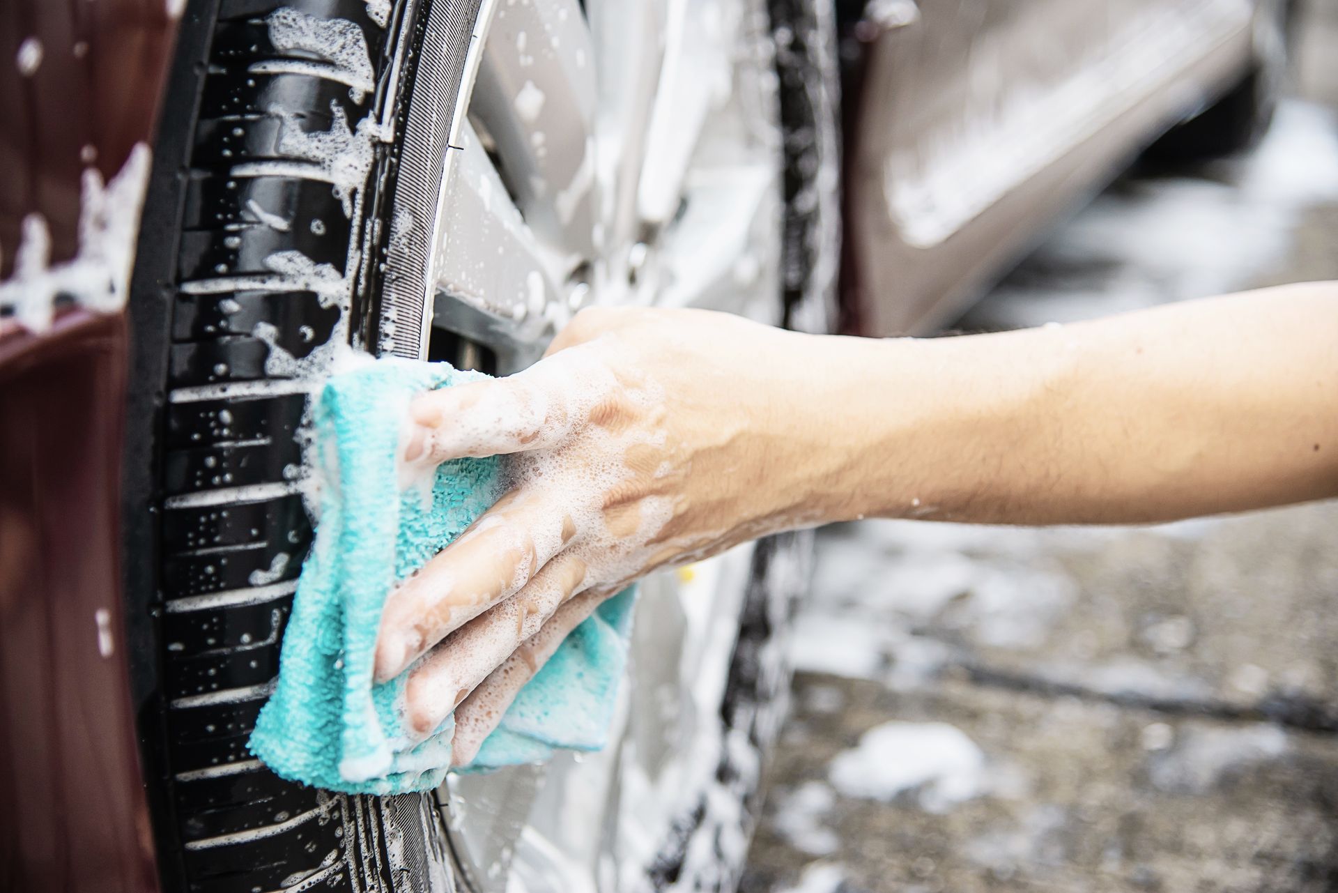 Hand washing a car tire with a blue sponge and soapy water