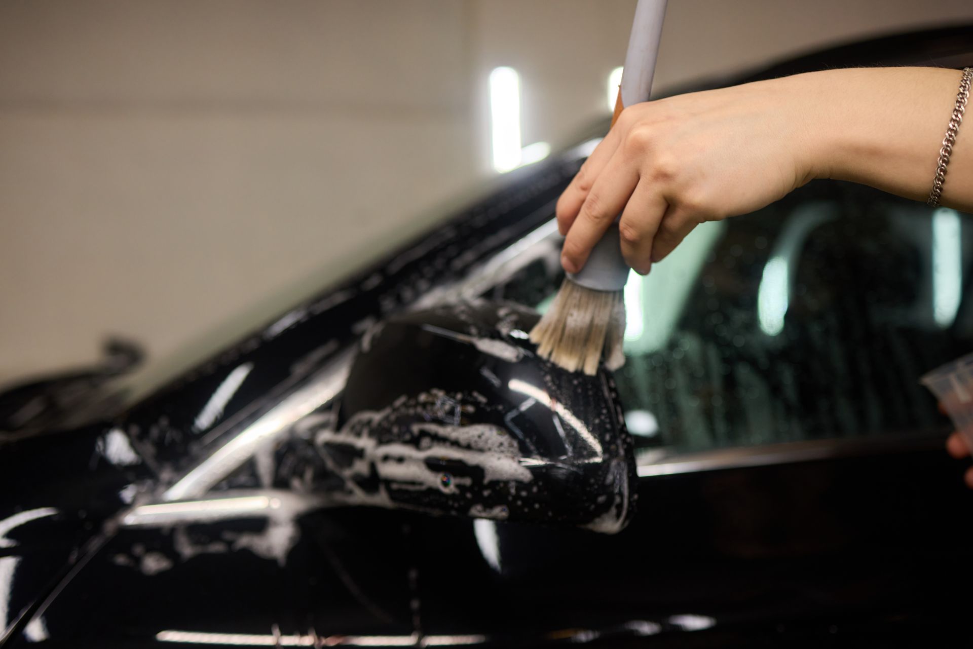 Hand washing a black car with a sponge, soap suds visible on the hood