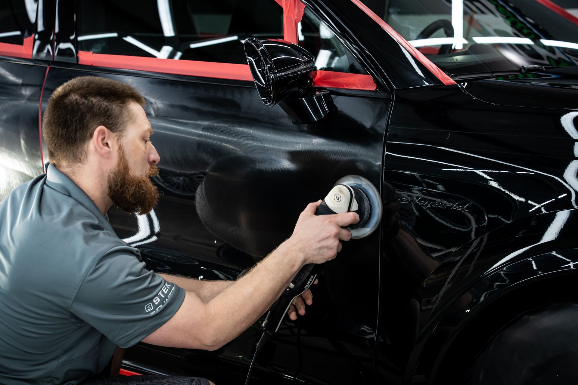 Mechanic polishing a black car door with a buffer in an auto shop