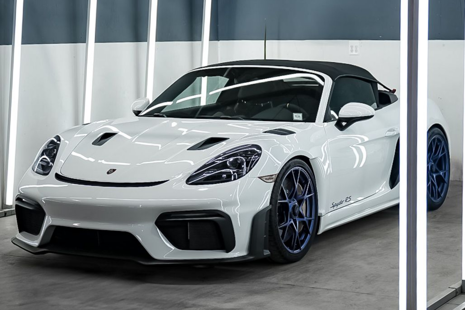 White sports car in a showroom, with a black roof and blue-rimmed wheels