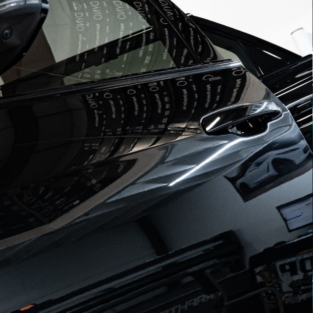 Close-up of a glossy black car door with reflections and a silver handle