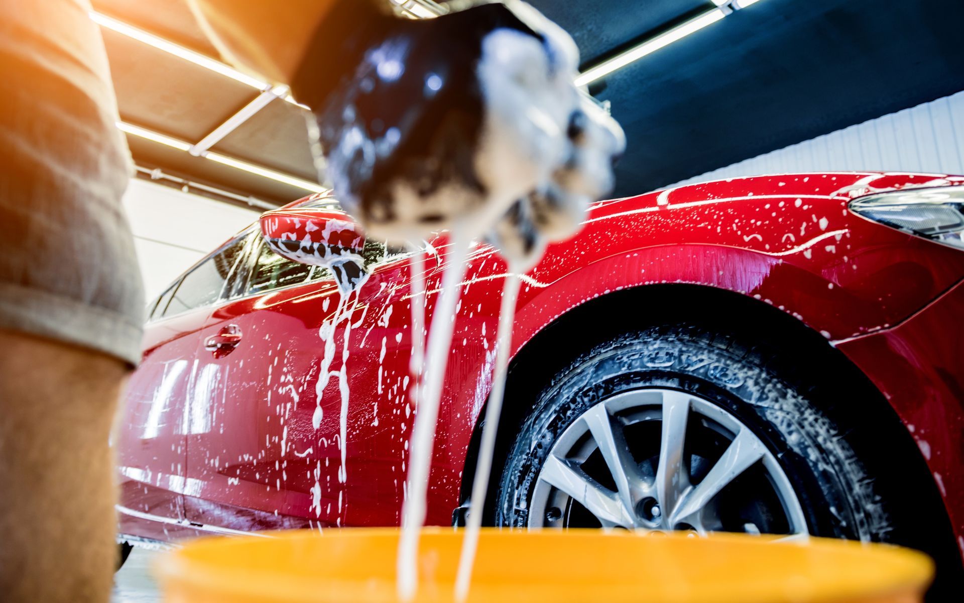 Person washing a red car with soap and water in a garage