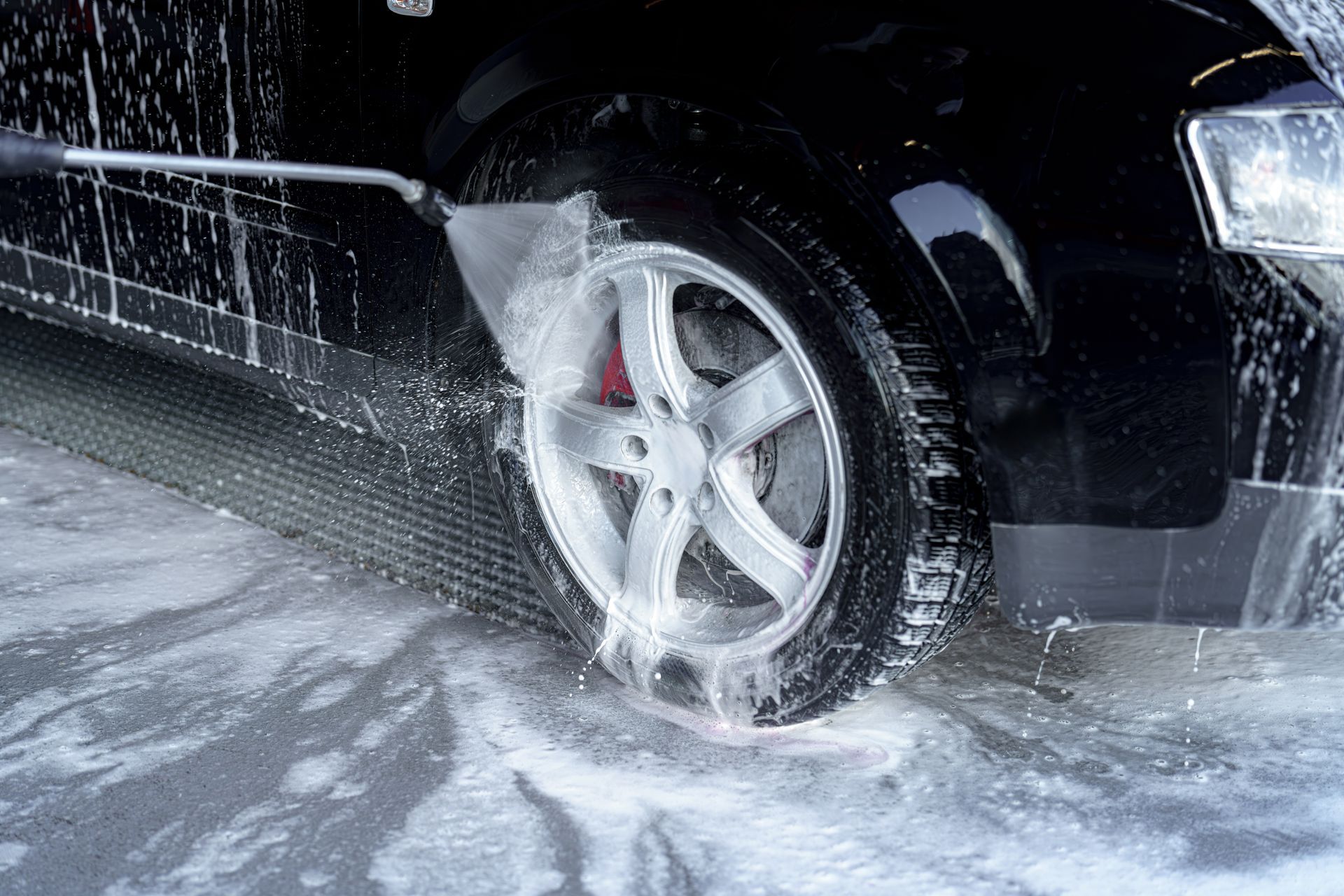 Black car tire spraying water on a wet road during a wash.