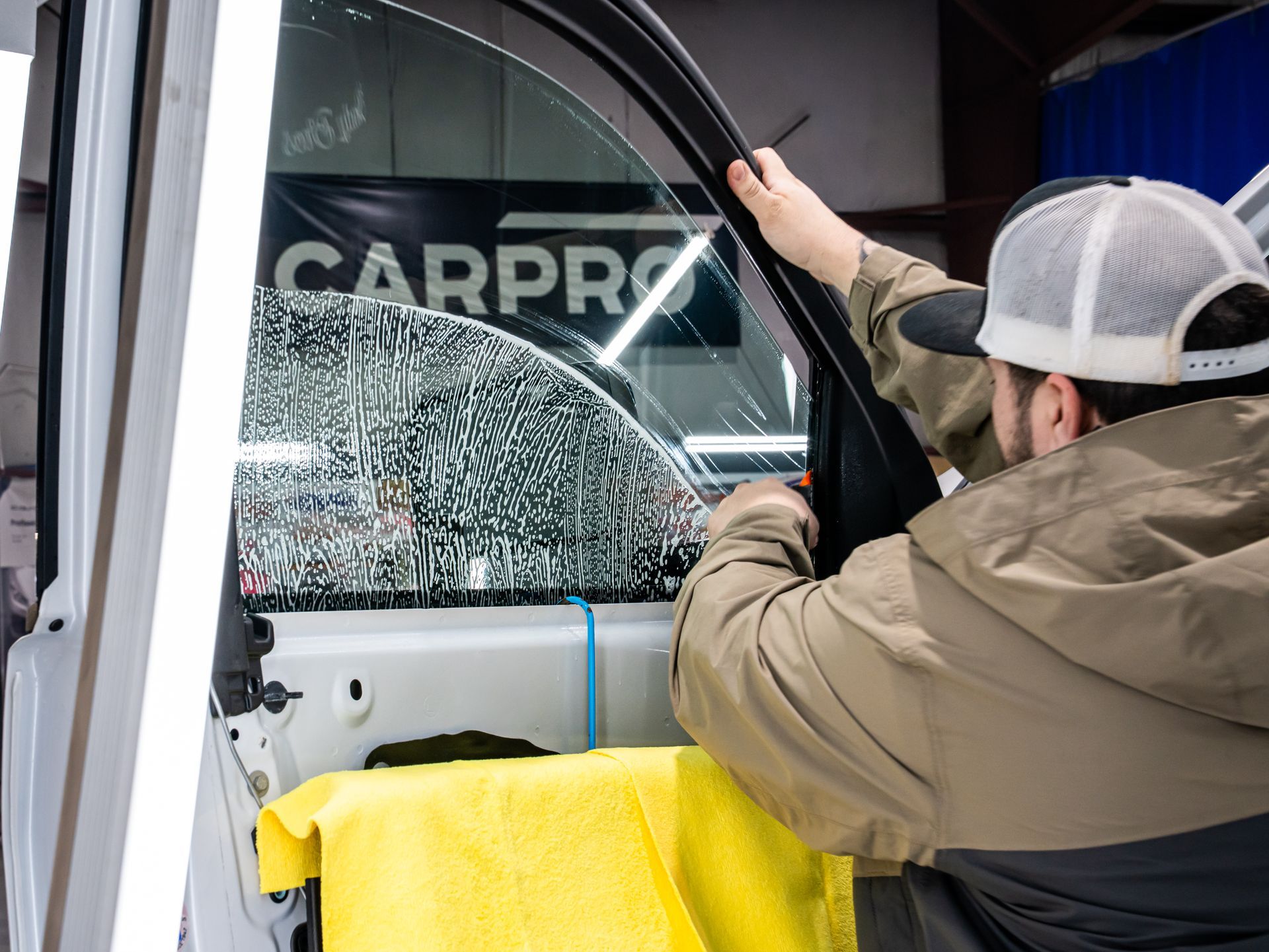 Technician installing a car window tint on a vehicle door with CARPRO branding visible