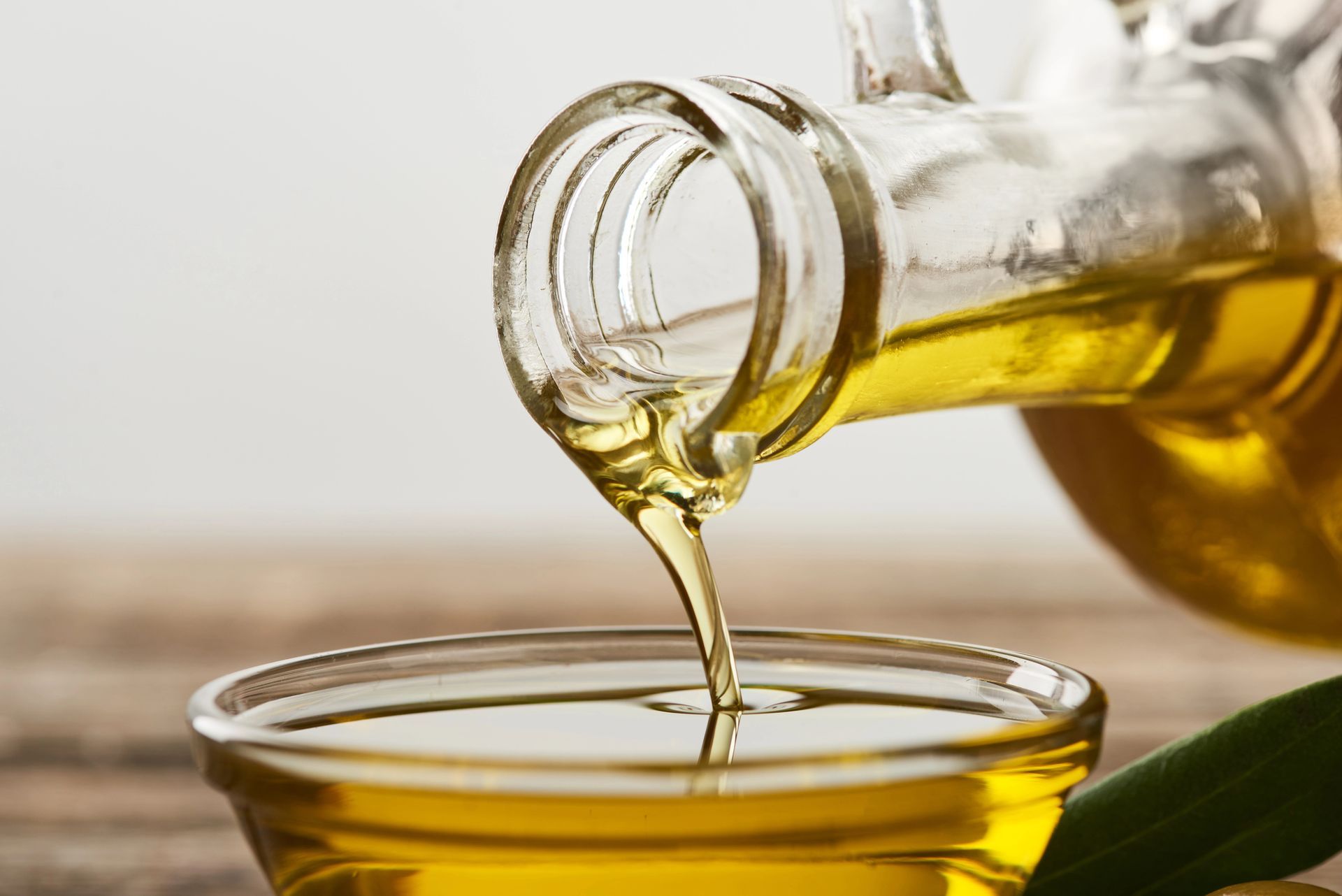Primo piano di olio d'oliva versato da una bottiglia di vetro in una piccola ciotola.