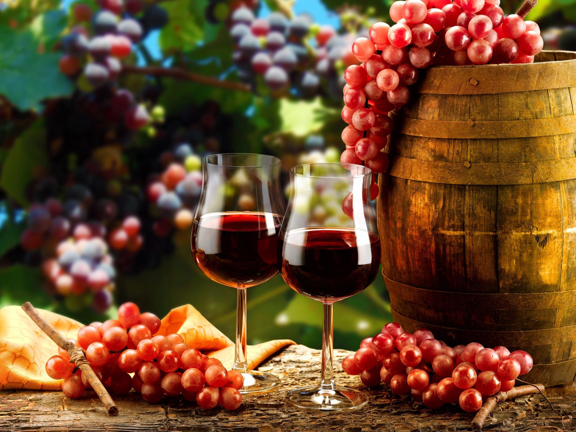 Due bicchieri di vino rosso accanto a una botte di legno e all'uva, all'aperto.