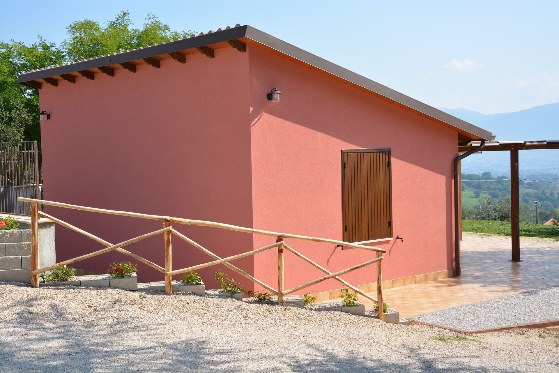 Edificio rosso con porta, recinzione e tetto marroni. All'esterno un patio chiaro.