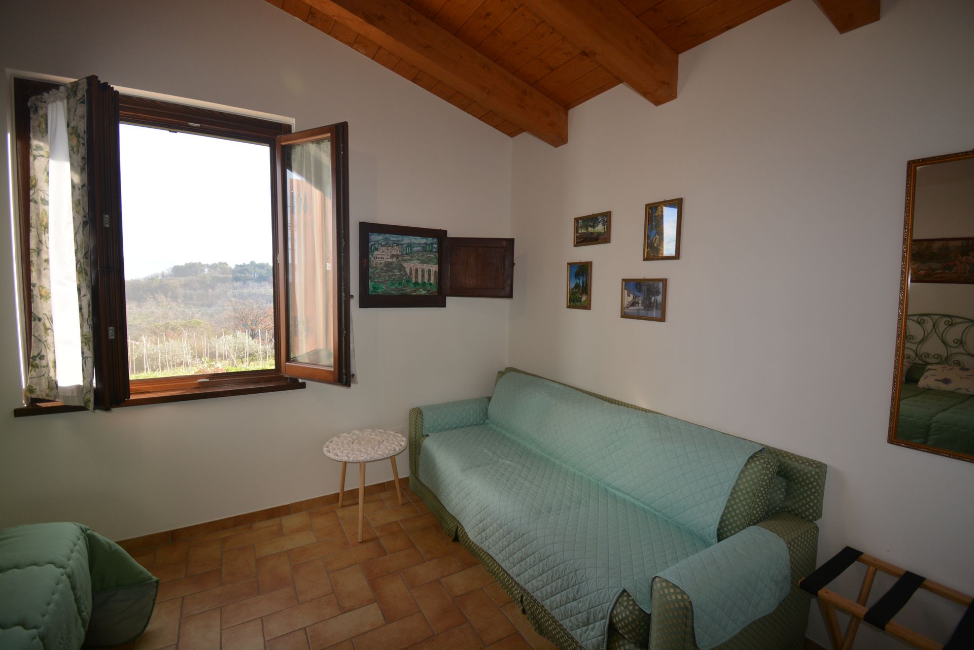 Piccola stanza con finestra, divano, tavolino e quadri alle pareti; tonalità azzurro chiaro e beige.