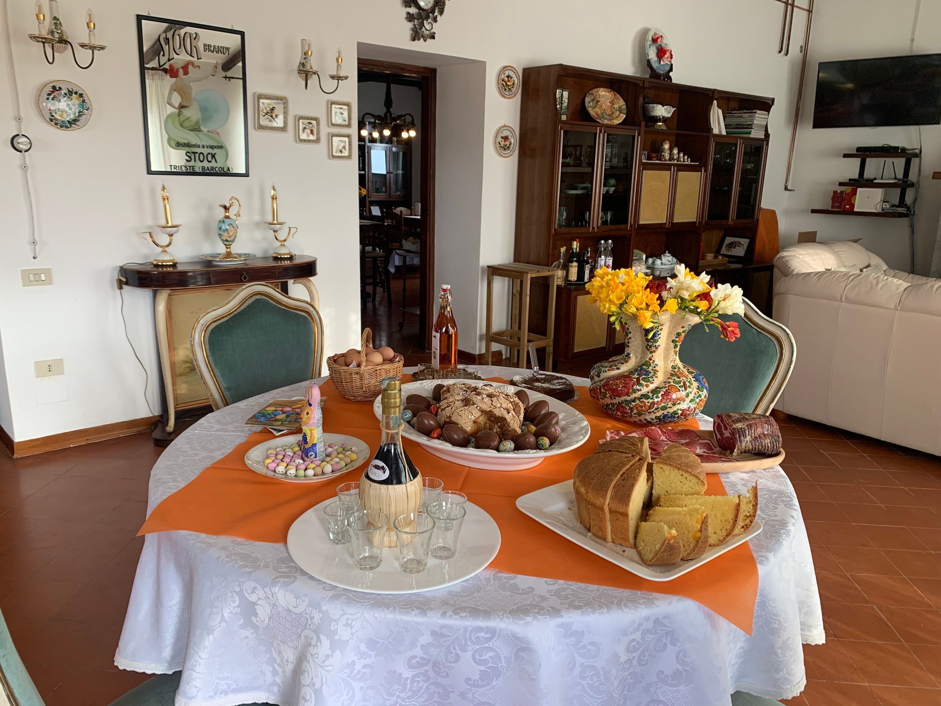 Una tavola imbandita con cibo e fiori in una sala da pranzo, con una tovaglia arancione e mobili decorativi.