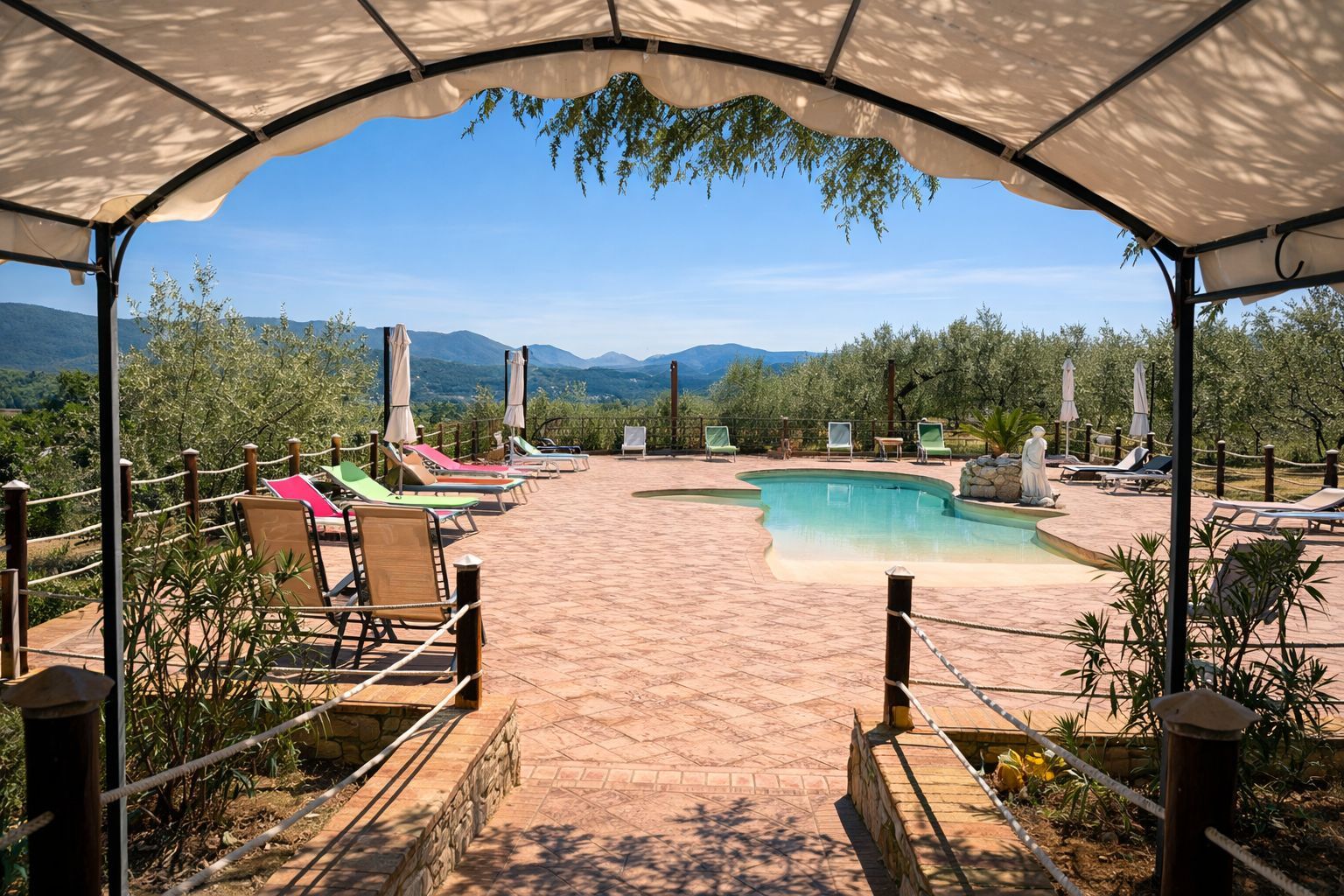 Piscina circondata da un patio in pietra e da ulivi sotto un cielo terso e azzurro.