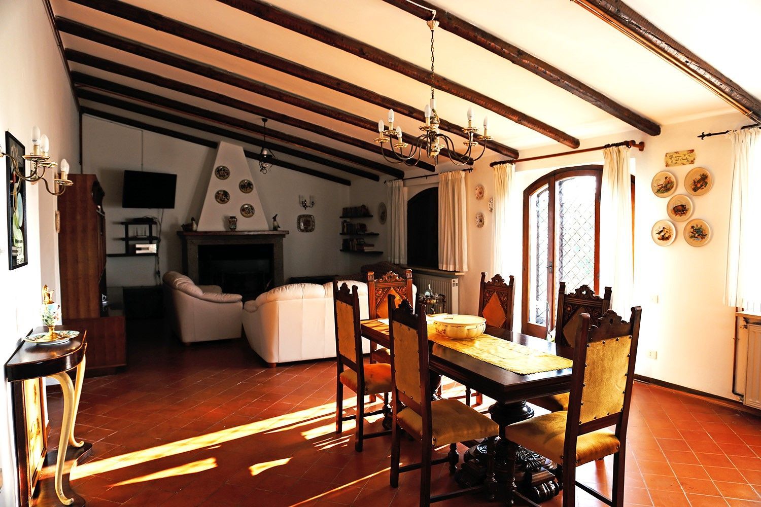 Soggiorno con travi in ​​legno, camino, tavolo da pranzo e ampia finestra.