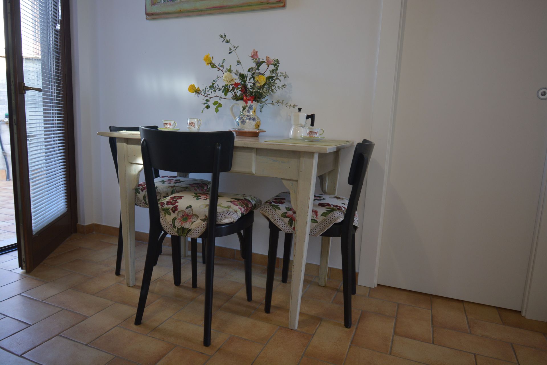 Un piccolo tavolo da pranzo con tre sedie, fiori e una porta.