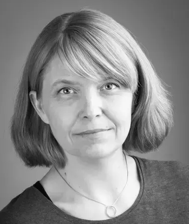 Woman with short blonde hair, in grayscale, smiling slightly, wearing a gray shirt and necklace.