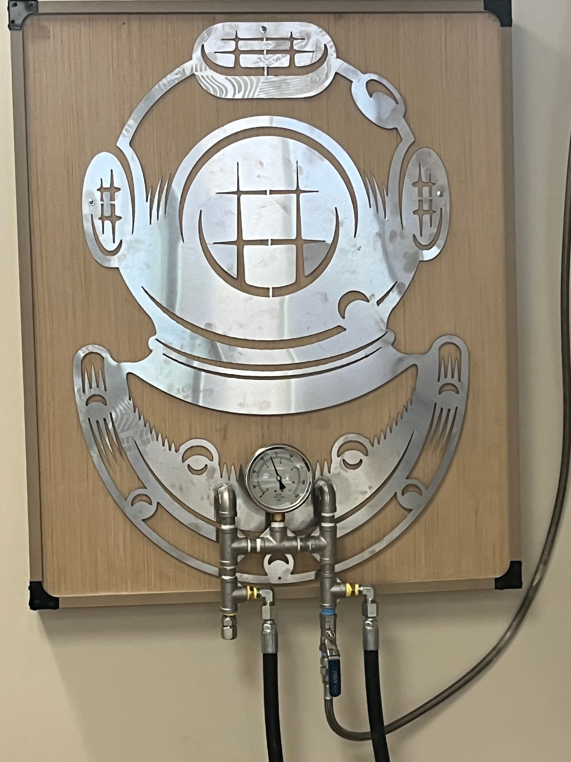 Metal marine-style wall art on wood panel above a small pipe fixture, in silver and beige tones