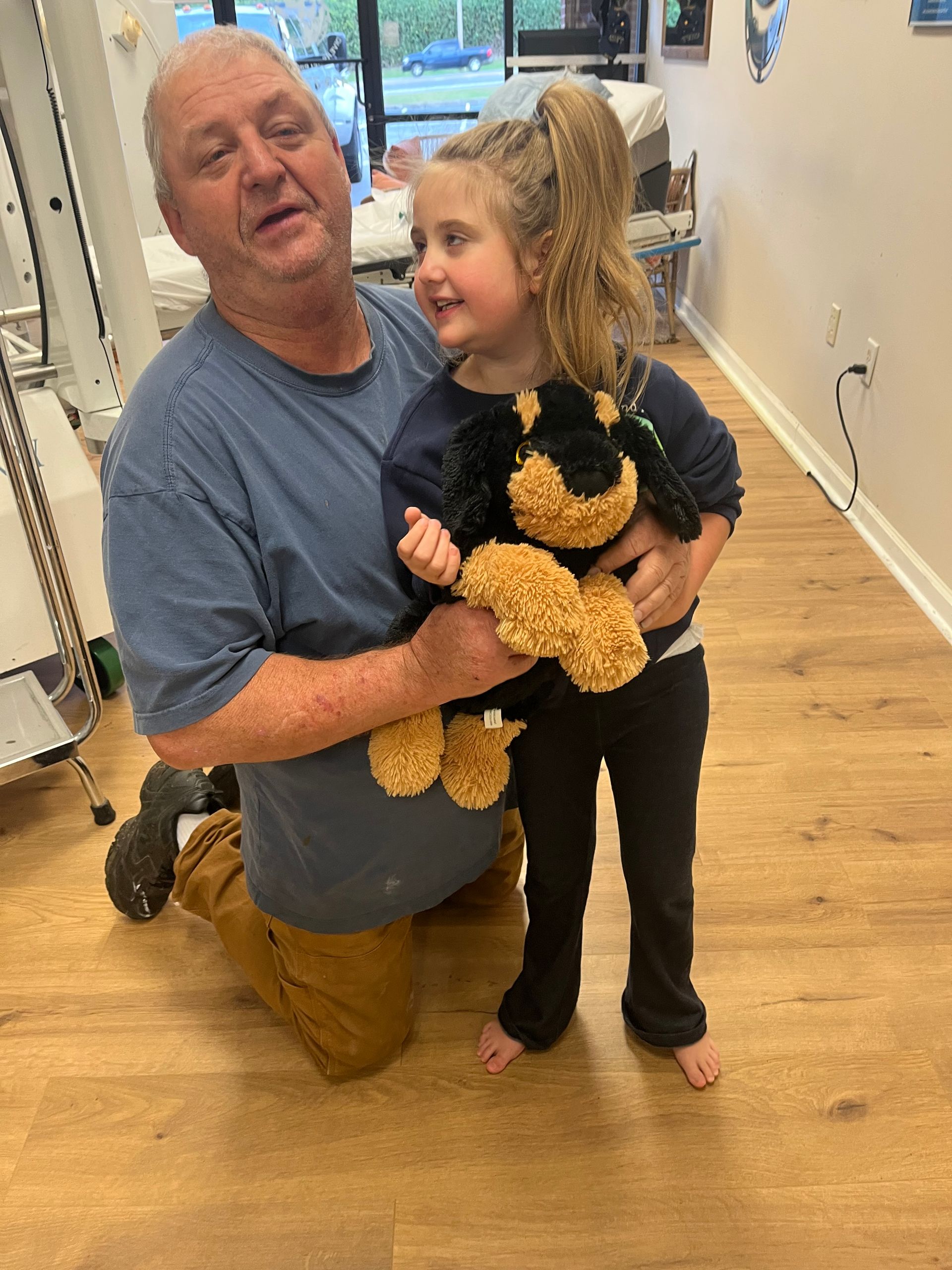 Man kneeling beside a smiling child holding a black-and-brown stuffed dog in a hallway