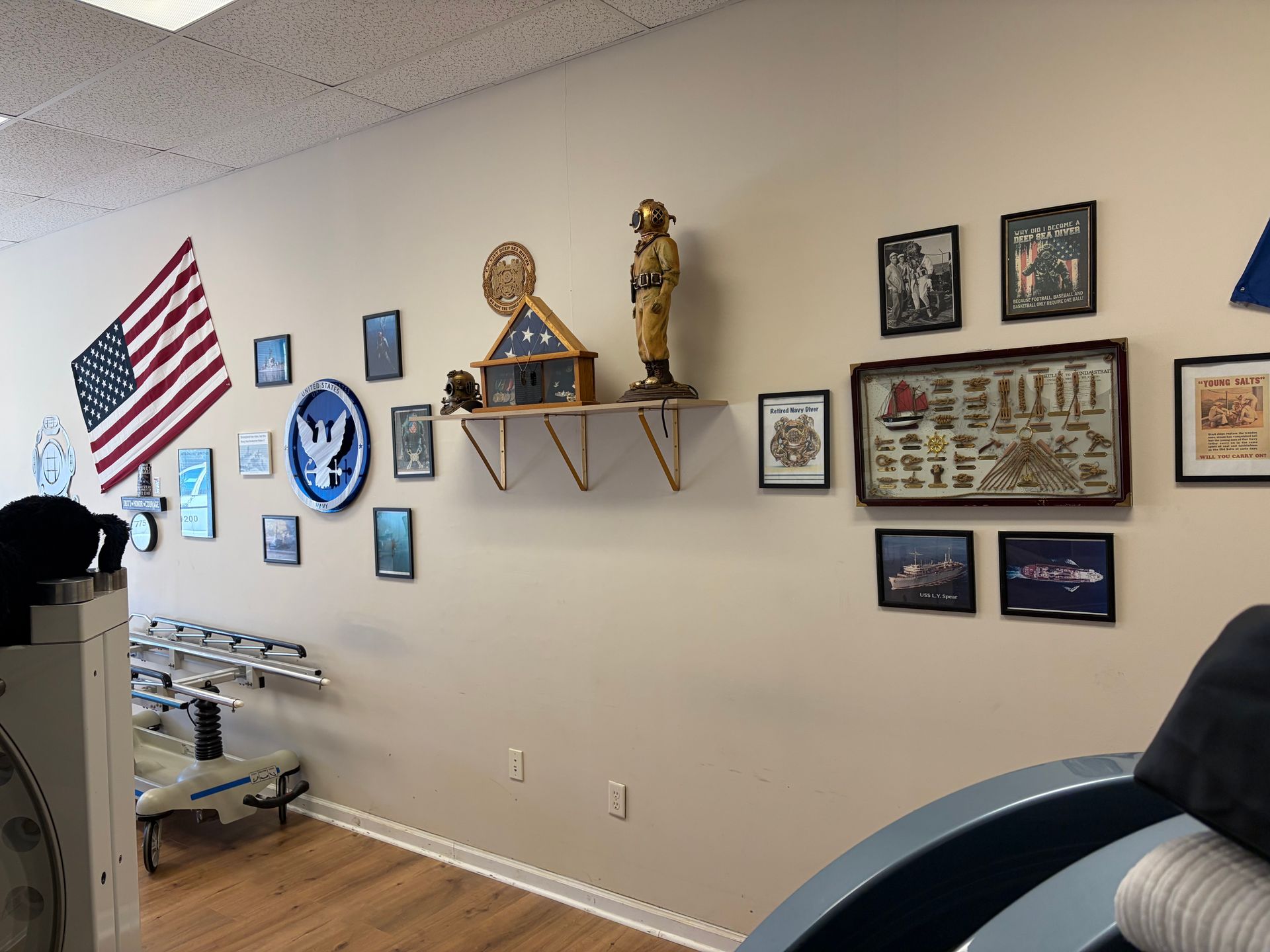 Wall decorated with American flag, plaques, framed photos, trophies, and shelves in a hallway.