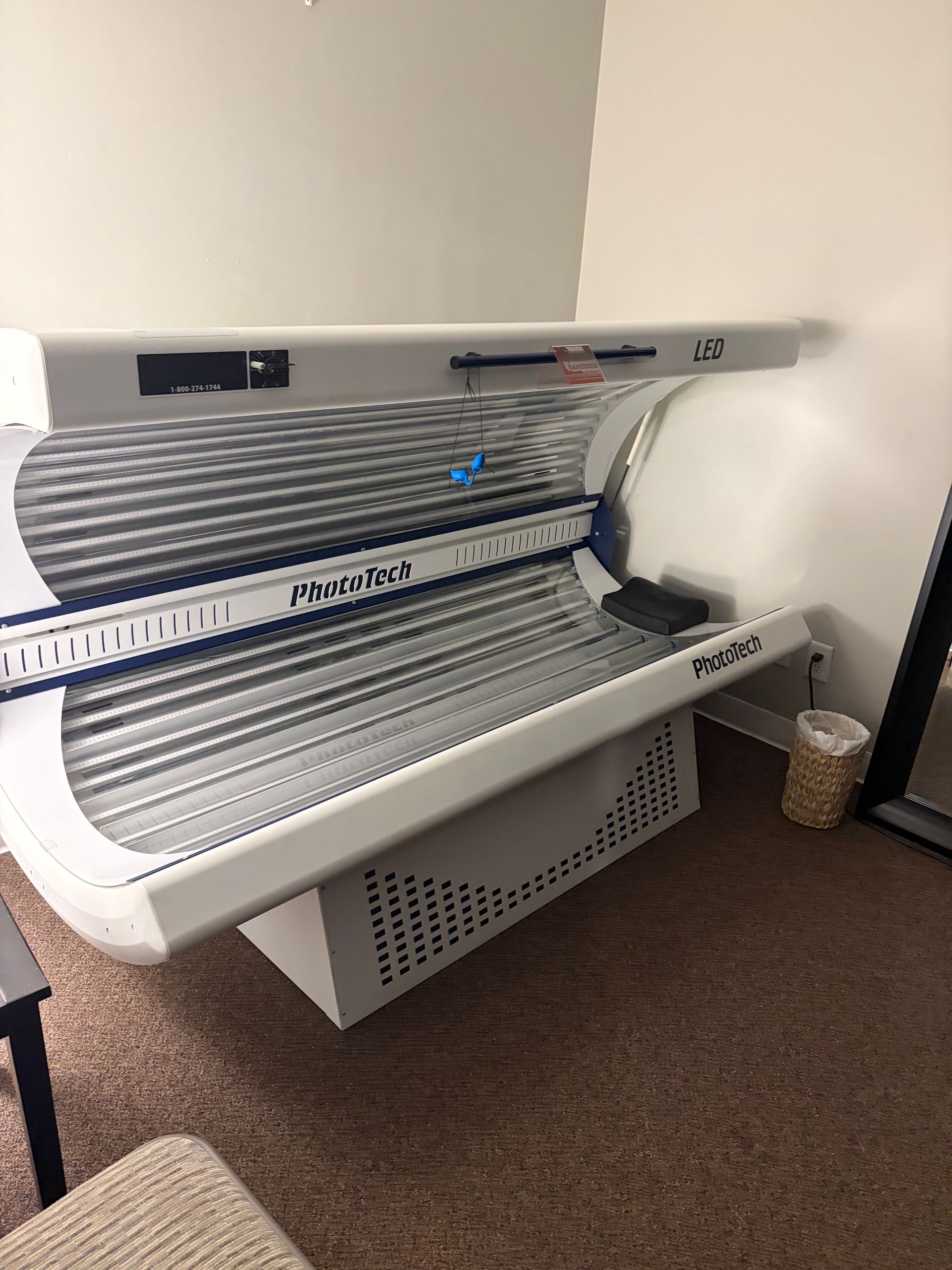 A tanning bed in a room with beige walls and carpet, with a small basket beside it.