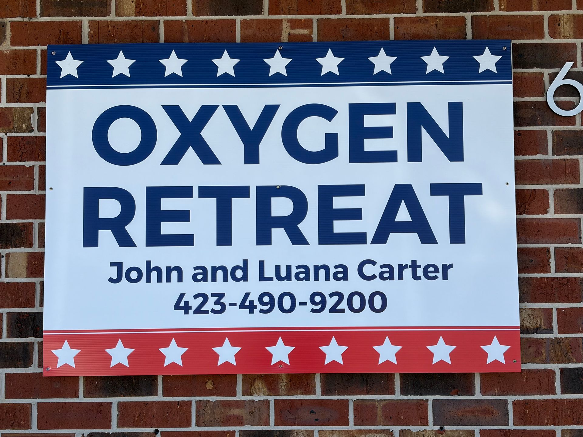 OXYGEN RETREAT sign with blue and red stars, listing Jhon and Luana Carter and phone number 423-490-9200