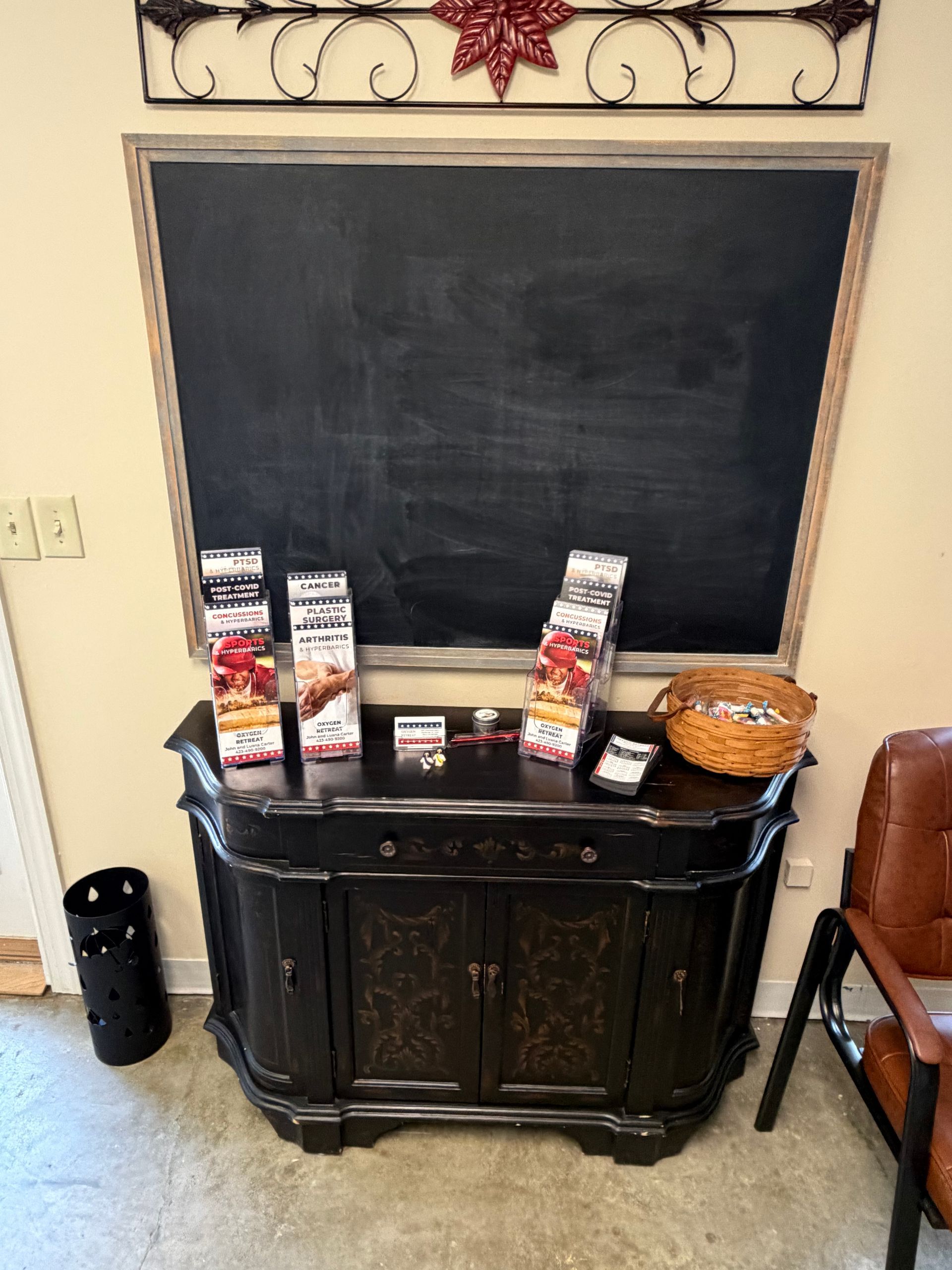 Black chalkboard above a dark wooden sideboard with brochures and a bowl in a room corner