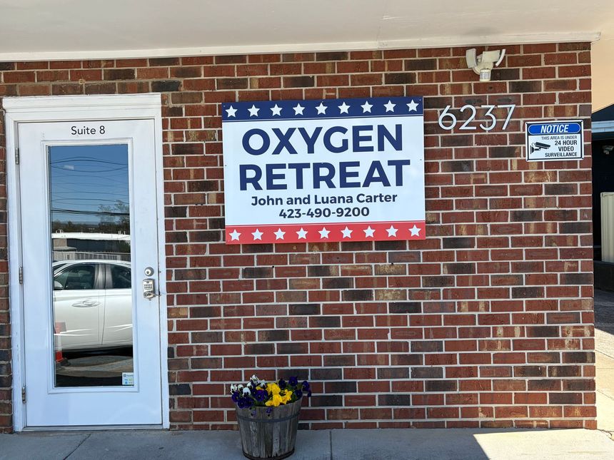 Brick storefront with an Oxygen Retreat sign and glass door, with a small flower pot by the entrance.