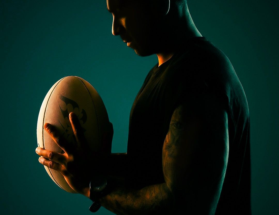 Person in silhouette holding a football against a dark teal background