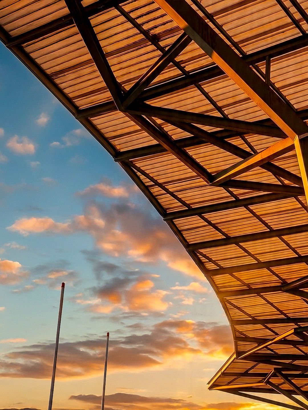 Sunset sky behind a metal canopy with orange beams and a few tall poles