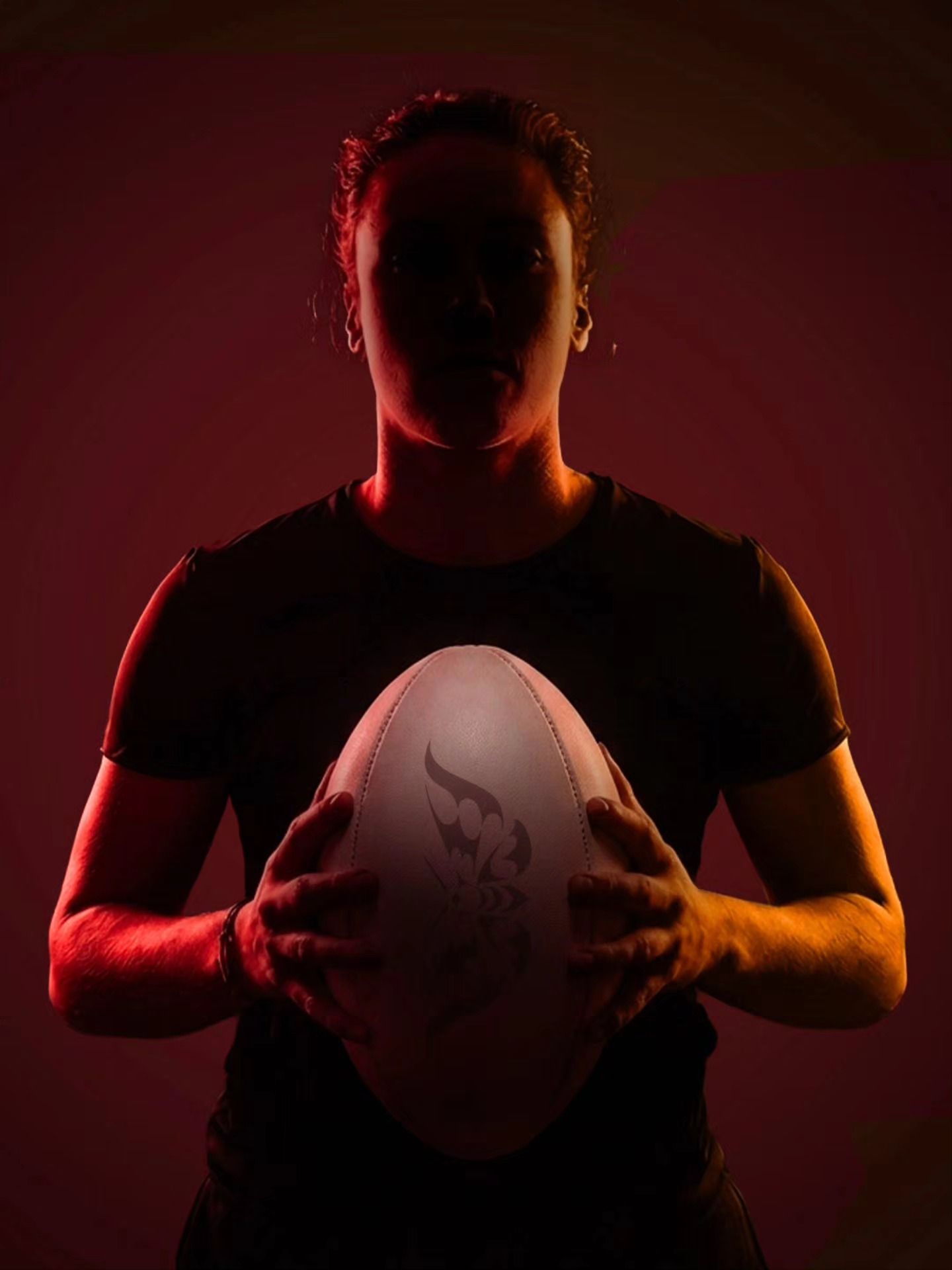 Person holding a rugby ball against a dark red-lit background
