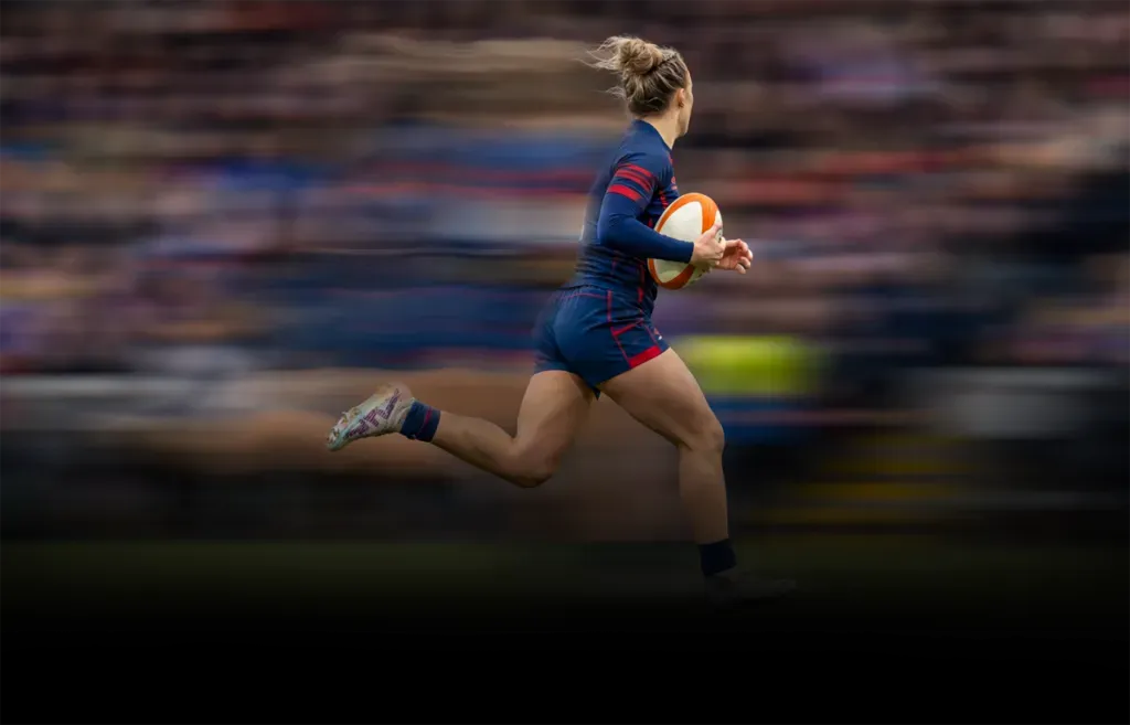 Rugby player in navy and red sprints with the ball across the field, motion blurred background