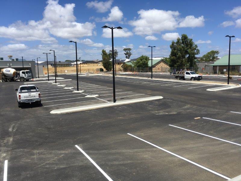 Empty paved parking lot with white parking lines and black streetlights under a blue sky, with parked trucks.
